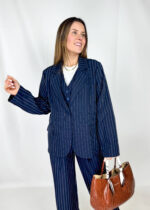 Una giacca gessata dal taglio oversize, dallo stile deciso e contemporaneo. La silhouette è ampia e strutturata, con spalle leggermente pronunciate e linea morbida che cade dritta lungo il busto. Il motivo gessato, con sottili righe verticali, richiama l’eleganza sartoriale classica, reinterpretata in chiave moderna. Presenta chiusura frontale con bottone, rever puliti e tasche a filetto