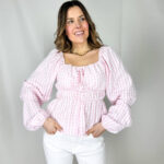 Fresca, romantica e di tendenza, questa camicetta crop è il capo ideale per un look leggero e femminile. Realizzata in morbido tessuto a quadratini rosa e bianchi, regala un’allure delicata e primaverile. Il modello corto con elastico in vita valorizza la silhouette creando un effetto leggermente blusato, mentre la balza sul fondo aggiunge movimento e un tocco sbarazzino. L’elastico sul collo permette di indossarla anche leggermente scesa sulle spalle per un look più romantico, completato dalle maniche ampie che donano volume e leggerezza.
