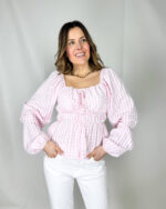 Fresca, romantica e di tendenza, questa camicetta crop è il capo ideale per un look leggero e femminile. Realizzata in morbido tessuto a quadratini rosa e bianchi, regala un’allure delicata e primaverile. Il modello corto con elastico in vita valorizza la silhouette creando un effetto leggermente blusato, mentre la balza sul fondo aggiunge movimento e un tocco sbarazzino. L’elastico sul collo permette di indossarla anche leggermente scesa sulle spalle per un look più romantico, completato dalle maniche ampie che donano volume e leggerezza.