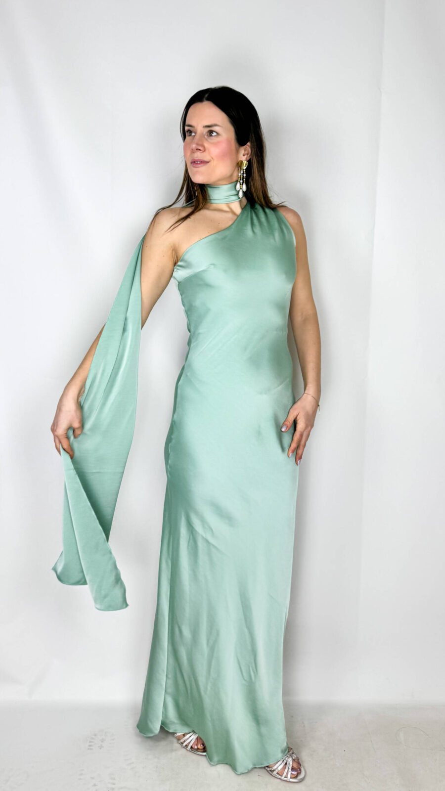 Abito lungo in satin color verde acqua delicato, raffinato e luminoso. Il modello monospalla dona un tocco sofisticato e moderno, mentre il morbido strascico può essere avvolto intorno al collo creando un elegante effetto drappeggiato. Il tessuto satinato scivola delicatamente lungo la silhouette, seguendo le linee del corpo con naturalezza e leggerezza. Perfetto per cerimonie, serate eleganti ed eventi speciali