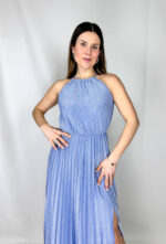 Abito da cerimonia lungo ed elegante, impreziosito da un raffinato tessuto brillantinato che illumina il look con discreta luminosità. Il modello presenta un girocollo alto con chiusura sul retro, che valorizza la linea del collo e dona un tocco sofisticato. Il corpetto plissettato crea movimento e leggerezza, mentre la gonna lunga fino alla caviglia è arricchita da un sensuale spacco che slancia la figura. L’elastico in vita garantisce comfort e una vestibilità adattabile, definendo delicatamente la silhouette. Perfetto per cerimonie, eventi eleganti e occasioni speciali.