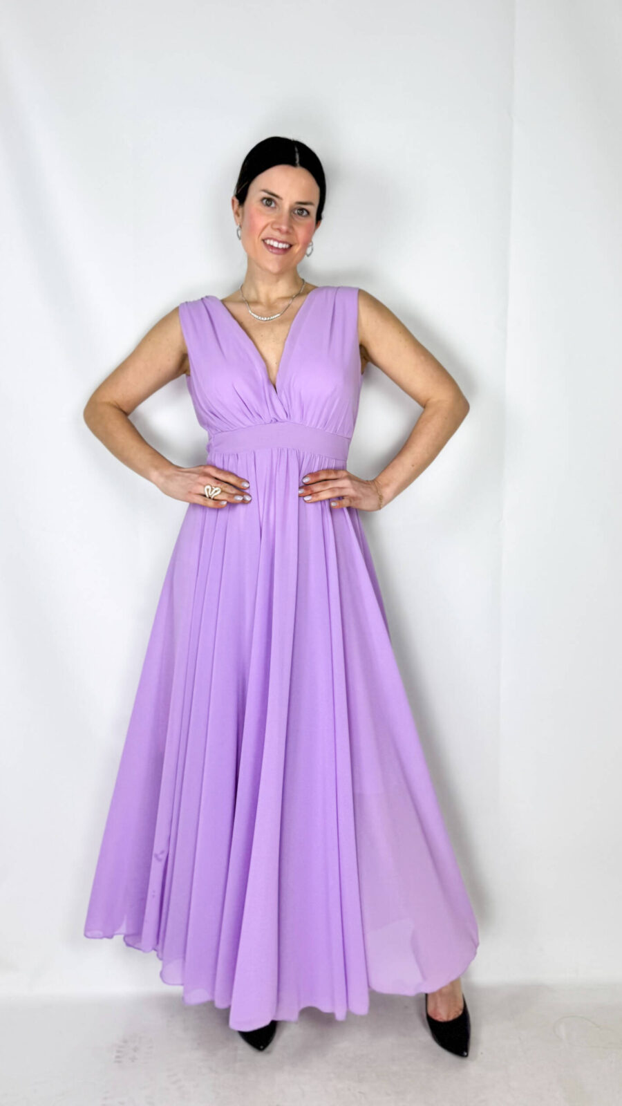 Abito romantico e femminile con scollo a V sia davanti che sul retro, che valorizza delicatamente il décolleté e la schiena. La vita con elastico definisce la silhouette garantendo comfort e vestibilità. La gonna è arricchita da una morbida sottogonna in cotone con strati di tulle color lilla che donano volume, leggerezza e un elegante effetto vaporoso. Perfetto per cerimonie, feste ed eventi speciali.