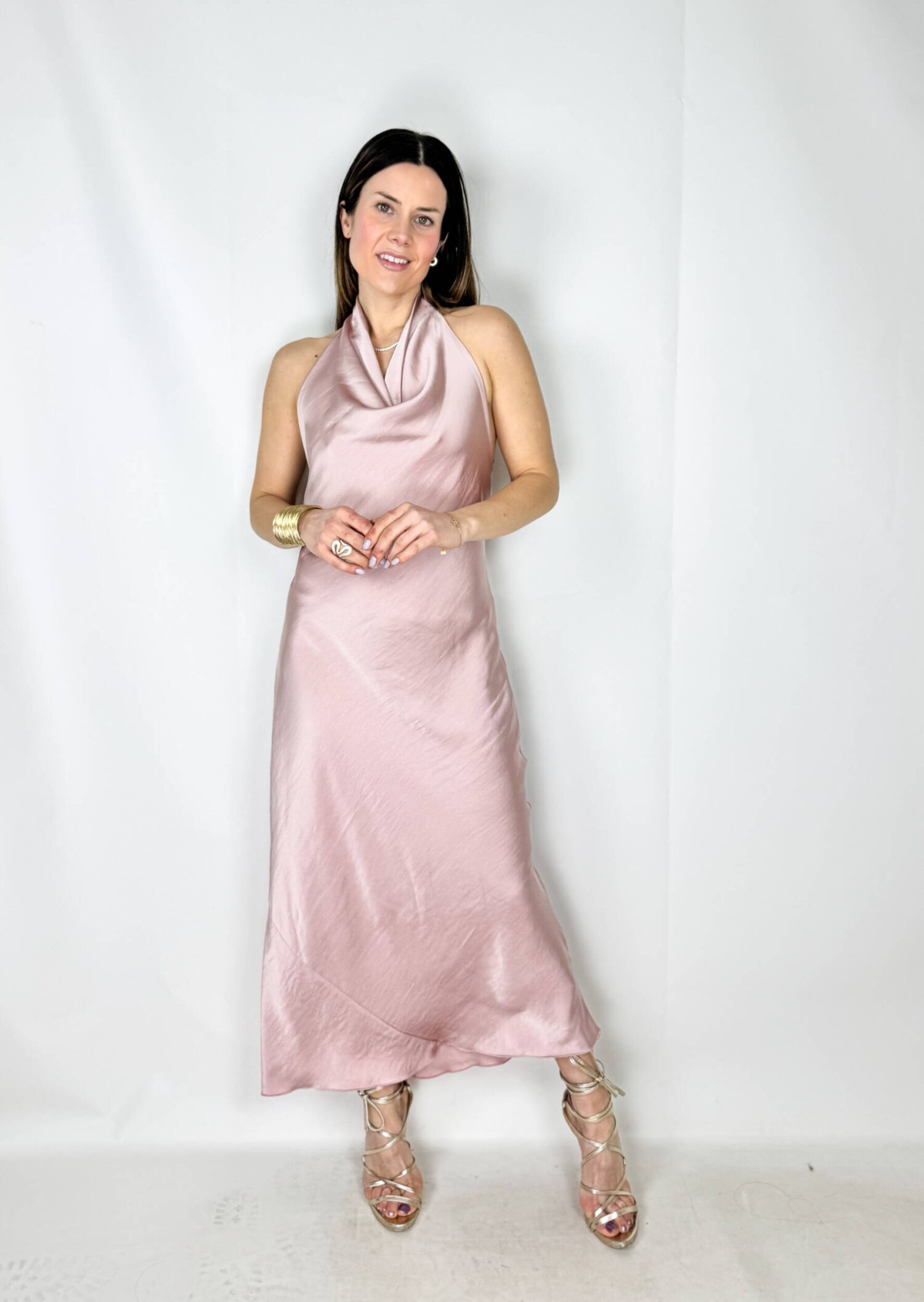 Abito lungo in satin color rosa, elegante e delicato. Il modello si allaccia dietro al collo lasciando la schiena leggermente scoperta, creando un effetto raffinato e femminile. Il tessuto satinato scende morbido lungo la silhouette fino alla caviglia, valorizzando le forme con naturalezza e leggerezza. Un abito romantico e sofisticato, perfetto per cerimonie, eventi eleganti e serate speciali.
