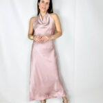 Abito lungo in satin color rosa, elegante e delicato. Il modello si allaccia dietro al collo lasciando la schiena leggermente scoperta, creando un effetto raffinato e femminile. Il tessuto satinato scende morbido lungo la silhouette fino alla caviglia, valorizzando le forme con naturalezza e leggerezza. Un abito romantico e sofisticato, perfetto per cerimonie, eventi eleganti e serate speciali.