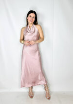 Abito lungo in satin color rosa, elegante e delicato. Il modello si allaccia dietro al collo lasciando la schiena leggermente scoperta, creando un effetto raffinato e femminile. Il tessuto satinato scende morbido lungo la silhouette fino alla caviglia, valorizzando le forme con naturalezza e leggerezza. Un abito romantico e sofisticato, perfetto per cerimonie, eventi eleganti e serate speciali.