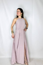 Abito da cerimonia lungo ed elegante, impreziosito da un raffinato tessuto brillantinato che illumina il look con discreta luminosità. Il modello presenta un girocollo alto con chiusura sul retro, che valorizza la linea del collo e dona un tocco sofisticato. Il corpetto plissettato crea movimento e leggerezza, mentre la gonna lunga fino alla caviglia è arricchita da un sensuale spacco che slancia la figura. L’elastico in vita garantisce comfort e una vestibilità adattabile, definendo delicatamente la silhouette. Perfetto per cerimonie, eventi eleganti e occasioni speciali.