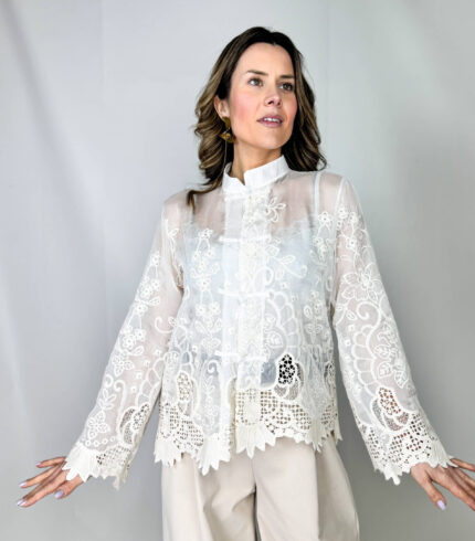 Camicia Japan elegante realizzata con un tessuto semi-trasparente, impreziosita dal ricamo floreale. Il collo alto leggermente strutturato aggiunge un tocco sofisticato mentre le maniche ampie terminano con polsini lavorati in pizzo.