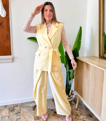 Coordinato dal carattere deciso e contemporaneo, pensato per chi ama distinguersi con eleganza. Il gilet doppiopetto è il protagonista assoluto: strutturato, con una linea sartoriale impeccabile, è impreziosito da bottoni dorati che decorano sia la chiusura frontale sia le spalline, aggiungendo un tocco sofisticato e distintivo. La cintura regolabile in vita valorizza la silhouette, permettendo una vestibilità personalizzata e femminile. Il pantalone a gamba larga completa il look con un’attitudine moderna e fluida. Caratterizzato da una doppia chiusura frontale, riprende il design dei modelli più iconici e di tendenza del 2026, offrendo una struttura pulita e un fit impeccabile.