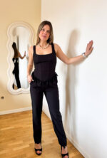 Coordinato nero essenziale e raffinato, perfetto per un look versatile e femminile. Il pantalone a gamba stretta valorizza la silhouette grazie alla linea aderente e alla vita elasticizzata, che garantisce comfort e vestibilità impeccabile per tutto il giorno. Il top completa il set con un tocco delicato e ricercato: caratterizzato da un elastico arricciato sulla schiena, si adatta perfettamente al corpo esaltando le forme con naturalezza. La balza in pizzo sul fondo aggiunge una nota romantica e sofisticata