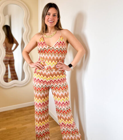 Tuta elasticizzata multicolore dallo stile vibrante e contemporaneo, ispirata alle iconiche fantasie zig-zag. Il design avvolgente valorizza la silhouette grazie al tessuto stretch che si adatta perfettamente al corpo, garantendo comfort e libertà di movimento. Il top a triangolo dona un’allure femminile e sensuale, mentre la schiena semi scoperta aggiunge un tocco audace e sofisticato, lasciando intravedere la pelle con eleganza. Il pantalone a gamba dritta completa il look con una linea fluida e slanciata, bilanciando perfettamente il fit aderente della parte superiore.