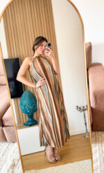 Abito lungo alla caviglia in tessuto plissettato dal fascino dinamico e luminoso. La fantasia multicolore, arricchita da una delicata finitura leggermente brillante, richiama uno stile sofisticato e contemporaneo ispirato alle iconiche lavorazioni a zig-zag. Il design presenta un elegante collo alto con allacciatura posteriore, che valorizza la linea delle spalle e dona un tocco raffinato e femminile. La silhouette è fluida e ariosa: il tessuto plissettato scende morbido e ampio lungo il corpo, creando movimento ad ogni passo.