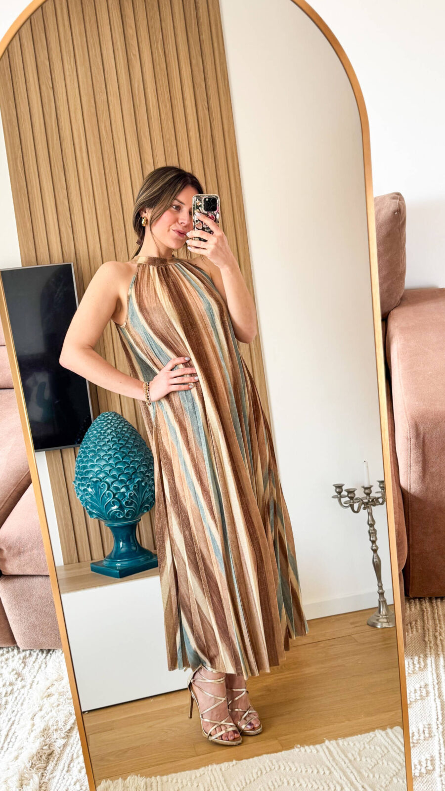 Abito lungo alla caviglia in tessuto plissettato dal fascino dinamico e luminoso. La fantasia multicolore, arricchita da una delicata finitura leggermente brillante, richiama uno stile sofisticato e contemporaneo ispirato alle iconiche lavorazioni a zig-zag. Il design presenta un elegante collo alto con allacciatura posteriore, che valorizza la linea delle spalle e dona un tocco raffinato e femminile. La silhouette è fluida e ariosa: il tessuto plissettato scende morbido e ampio lungo il corpo, creando movimento ad ogni passo.