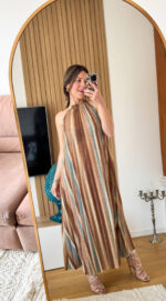 Abito lungo alla caviglia in tessuto plissettato dal fascino dinamico e luminoso. La fantasia multicolore, arricchita da una delicata finitura leggermente brillante, richiama uno stile sofisticato e contemporaneo ispirato alle iconiche lavorazioni a zig-zag. Il design presenta un elegante collo alto con allacciatura posteriore, che valorizza la linea delle spalle e dona un tocco raffinato e femminile. La silhouette è fluida e ariosa: il tessuto plissettato scende morbido e ampio lungo il corpo, creando movimento ad ogni passo.