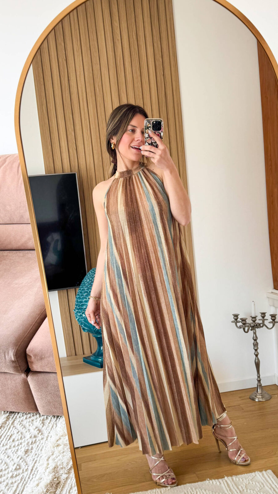 Abito lungo alla caviglia in tessuto plissettato dal fascino dinamico e luminoso. La fantasia multicolore, arricchita da una delicata finitura leggermente brillante, richiama uno stile sofisticato e contemporaneo ispirato alle iconiche lavorazioni a zig-zag. Il design presenta un elegante collo alto con allacciatura posteriore, che valorizza la linea delle spalle e dona un tocco raffinato e femminile. La silhouette è fluida e ariosa: il tessuto plissettato scende morbido e ampio lungo il corpo, creando movimento ad ogni passo.