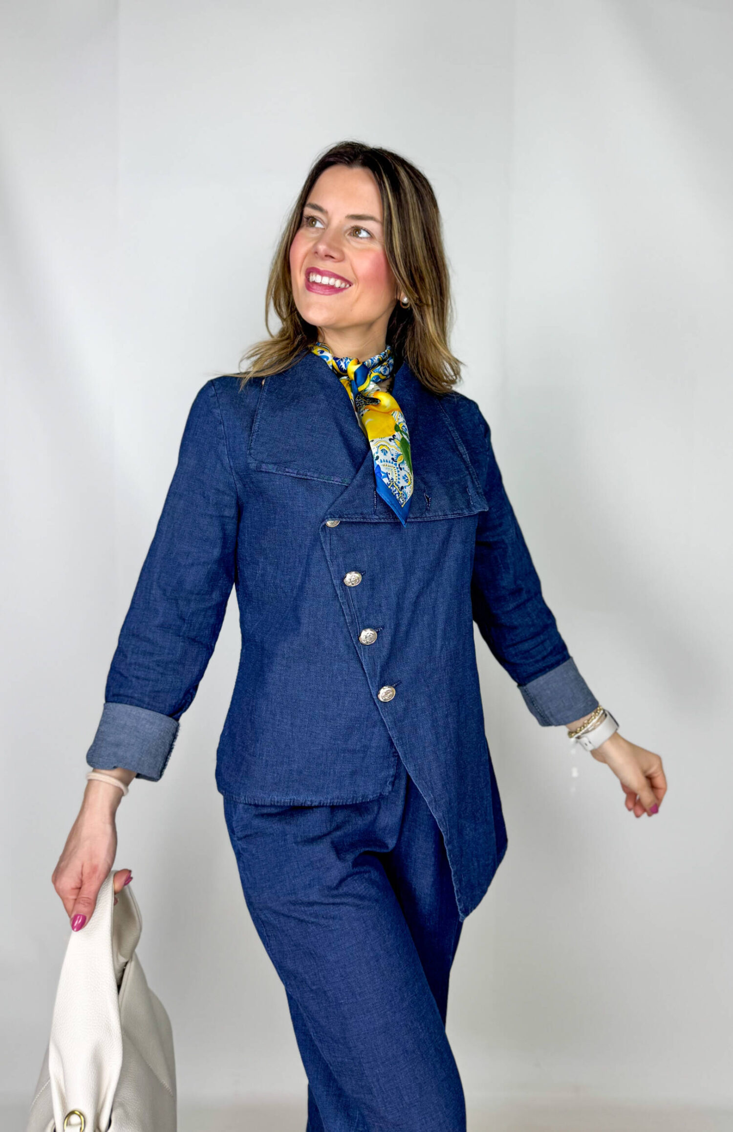 Coordinato in leggero denim primaverile, fresco e contemporaneo, ideale per la mezza stagione. Il pantalone, con elastico in vita, presenta una linea morbida a ovetto che avvolge la silhouette con comfort e stile. La giacca, dal design originale, si chiude frontalmente in modo trasversale ed è impreziosita da bottoni dorati che aggiungono un tocco luminoso e sofisticato. Un completo moderno e ricercato, perfetto per look casual-chic dal carattere distintivo.