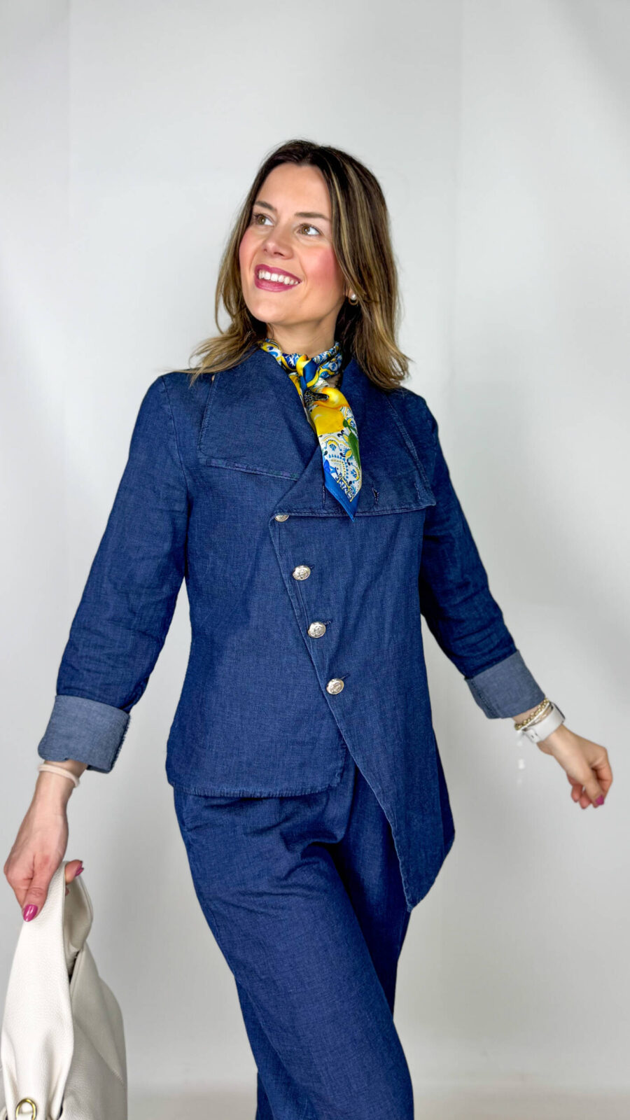 Coordinato in leggero denim primaverile, fresco e contemporaneo, ideale per la mezza stagione. Il pantalone, con elastico in vita, presenta una linea morbida a ovetto che avvolge la silhouette con comfort e stile. La giacca, dal design originale, si chiude frontalmente in modo trasversale ed è impreziosita da bottoni dorati che aggiungono un tocco luminoso e sofisticato. Un completo moderno e ricercato, perfetto per look casual-chic dal carattere distintivo.