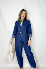 Coordinato in leggero denim primaverile, fresco e contemporaneo, ideale per la mezza stagione. Il pantalone, con elastico in vita, presenta una linea morbida a ovetto che avvolge la silhouette con comfort e stile. La giacca, dal design originale, si chiude frontalmente in modo trasversale ed è impreziosita da bottoni dorati che aggiungono un tocco luminoso e sofisticato. Un completo moderno e ricercato, perfetto per look casual-chic dal carattere distintivo.