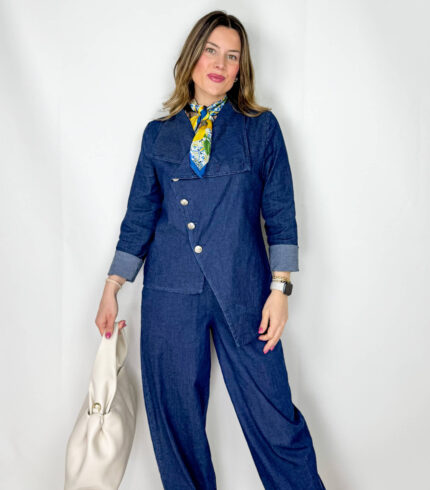Coordinato in leggero denim primaverile, fresco e contemporaneo, ideale per la mezza stagione. Il pantalone, con elastico in vita, presenta una linea morbida a ovetto che avvolge la silhouette con comfort e stile. La giacca, dal design originale, si chiude frontalmente in modo trasversale ed è impreziosita da bottoni dorati che aggiungono un tocco luminoso e sofisticato. Un completo moderno e ricercato, perfetto per look casual-chic dal carattere distintivo.
