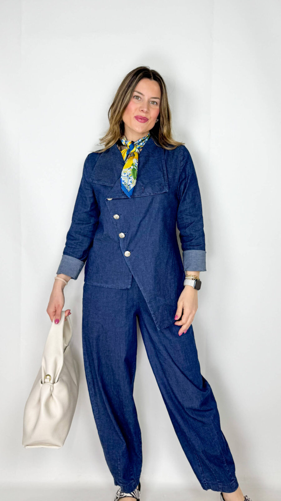 Coordinato in leggero denim primaverile, fresco e contemporaneo, ideale per la mezza stagione. Il pantalone, con elastico in vita, presenta una linea morbida a ovetto che avvolge la silhouette con comfort e stile. La giacca, dal design originale, si chiude frontalmente in modo trasversale ed è impreziosita da bottoni dorati che aggiungono un tocco luminoso e sofisticato. Un completo moderno e ricercato, perfetto per look casual-chic dal carattere distintivo.