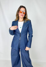 Coordinato in tessuto denim dal carattere deciso e contemporaneo, pensato per un look strutturato ma estremamente versatile. Il pantalone a palazzo scivola ampio lungo la gamba, slanciando la figura e garantendo comfort e movimento. La giacca, chiusa in vita con eleganti gancetti, valorizza la silhouette creando un raffinato contrasto tra volumi. Le spalline imbottite e più pronunciate aggiungono un tocco grintoso e sofisticato, ispirato a linee sartoriali moderne. Un completo perfetto per distinguersi con stile, ideale sia per il giorno che per la sera.