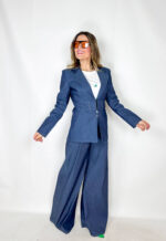 Coordinato in tessuto denim dal carattere deciso e contemporaneo, pensato per un look strutturato ma estremamente versatile. Il pantalone a palazzo scivola ampio lungo la gamba, slanciando la figura e garantendo comfort e movimento. La giacca, chiusa in vita con eleganti gancetti, valorizza la silhouette creando un raffinato contrasto tra volumi. Le spalline imbottite e più pronunciate aggiungono un tocco grintoso e sofisticato, ispirato a linee sartoriali moderne. Un completo perfetto per distinguersi con stile, ideale sia per il giorno che per la sera.