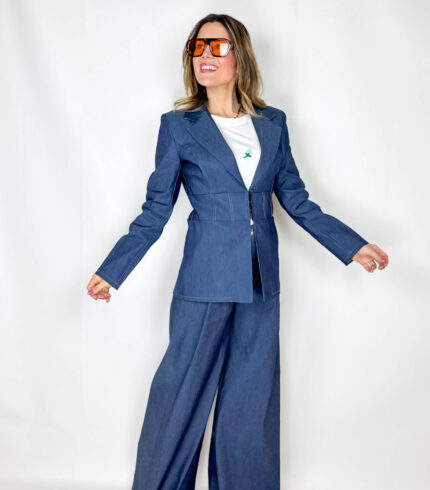 Coordinato in tessuto denim dal carattere deciso e contemporaneo, pensato per un look strutturato ma estremamente versatile. Il pantalone a palazzo scivola ampio lungo la gamba, slanciando la figura e garantendo comfort e movimento. La giacca, chiusa in vita con eleganti gancetti, valorizza la silhouette creando un raffinato contrasto tra volumi. Le spalline imbottite e più pronunciate aggiungono un tocco grintoso e sofisticato, ispirato a linee sartoriali moderne. Un completo perfetto per distinguersi con stile, ideale sia per il giorno che per la sera.