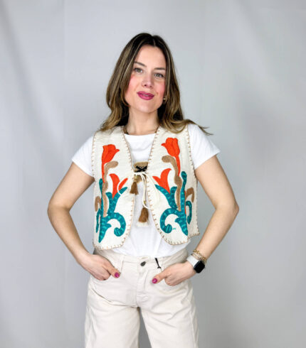Gilet in 100% cotone, interamente realizzato a mano, espressione di artigianalità e cura per i dettagli. La superficie è arricchita da ricami colorati che donano vivacità e unicità al capo, rendendolo un vero pezzo distintivo. La chiusura con asola sul petto aggiunge un tocco delicato e funzionale