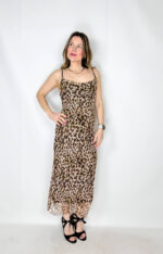 Abito lungo in fantasia leopardata, realizzato in tessuto elasticizzato che avvolge la silhouette esaltandone le forme con naturale eleganza. Il modello presenta uno scollo a barchetta raffinato, che valorizza le spalle, mentre la schiena leggermente scoperta aggiunge un tocco sensuale e sofisticato. La lunghezza alla caviglia slancia la figura, rendendo il capo ideale sia per il giorno che per la sera.