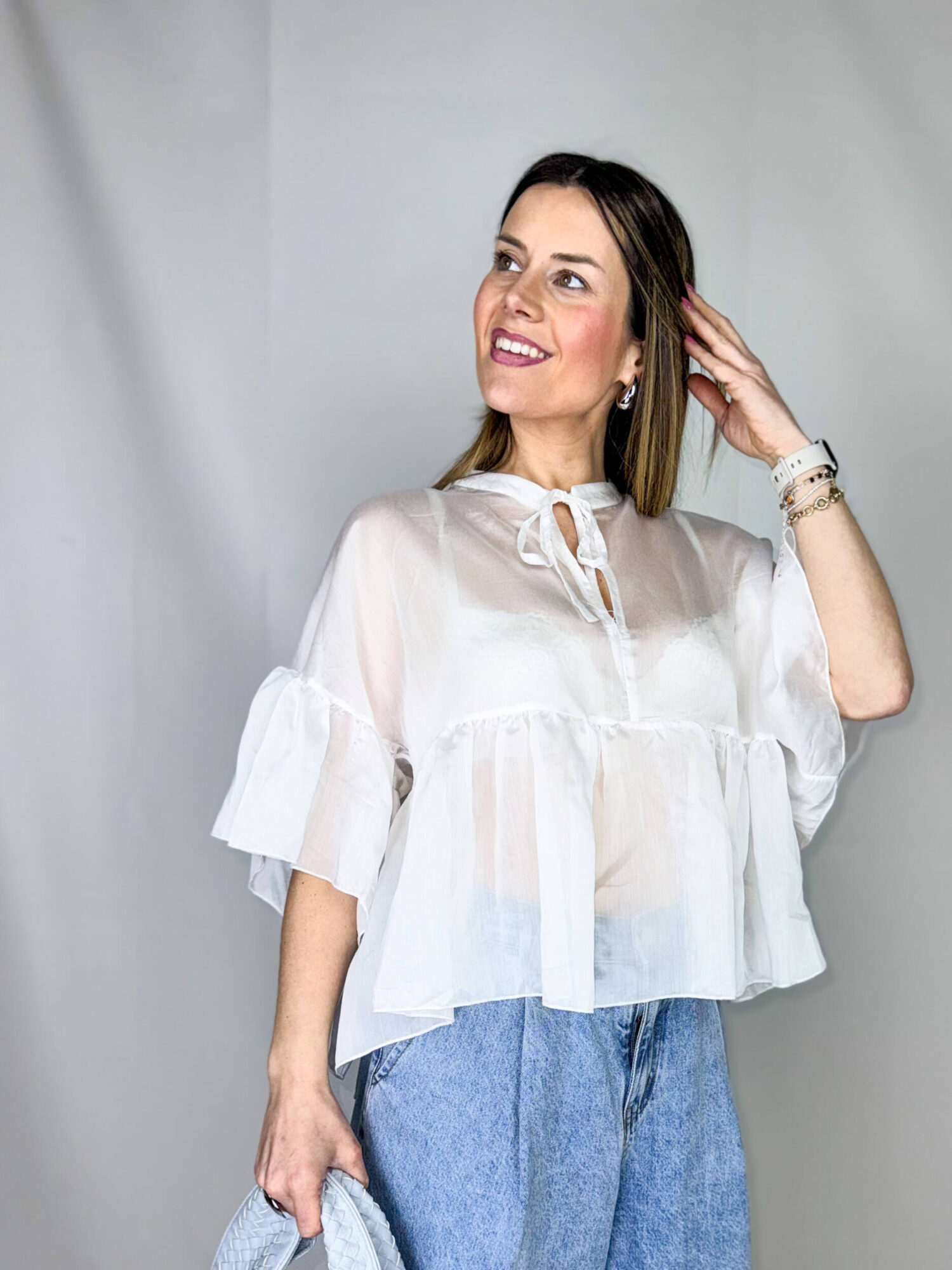 Blusa leggera e raffinata realizzata in morbido tencel velato, dal fascino etereo e contemporaneo. Il design è valorizzato da una delicata balza sul fondo che dona movimento e femminilità alla silhouette. Le maniche corte a palloncino aggiungono volume e un tocco romantico, mentre il collo alla coreana conferisce un’eleganza essenziale e pulita. Sul davanti, un’apertura a goccia impreziosita da un fiocchetto completa il capo