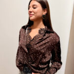 Camicia femminile in misto viscosa, morbida e piacevole al tatto, caratterizzata da una raffinata fantasia marrone scuro con piccoli dettagli luminosi. Il modello presenta un elegante colletto con scollo a V, maniche lunghe e una vestibilità morbida e fluida che valorizza la silhouette senza risultare aderente. Il dettaglio del nodo sul davanti dona un tocco moderno e rende il capo particolarmente femminile e ricercato. I dettagli decorativi sul colletto e lungo la parte frontale aggiungono carattere alla fantasia. Perfetta da abbinare a jeans, pantaloni sartoriali o gonne, è ideale sia per un look quotidiano curato sia per un outfit più elegante.