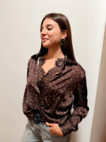 Camicia femminile in misto viscosa, morbida e piacevole al tatto, caratterizzata da una raffinata fantasia marrone scuro con piccoli dettagli luminosi. Il modello presenta un elegante colletto con scollo a V, maniche lunghe e una vestibilità morbida e fluida che valorizza la silhouette senza risultare aderente. Il dettaglio del nodo sul davanti dona un tocco moderno e rende il capo particolarmente femminile e ricercato. I dettagli decorativi sul colletto e lungo la parte frontale aggiungono carattere alla fantasia. Perfetta da abbinare a jeans, pantaloni sartoriali o gonne, è ideale sia per un look quotidiano curato sia per un outfit più elegante.