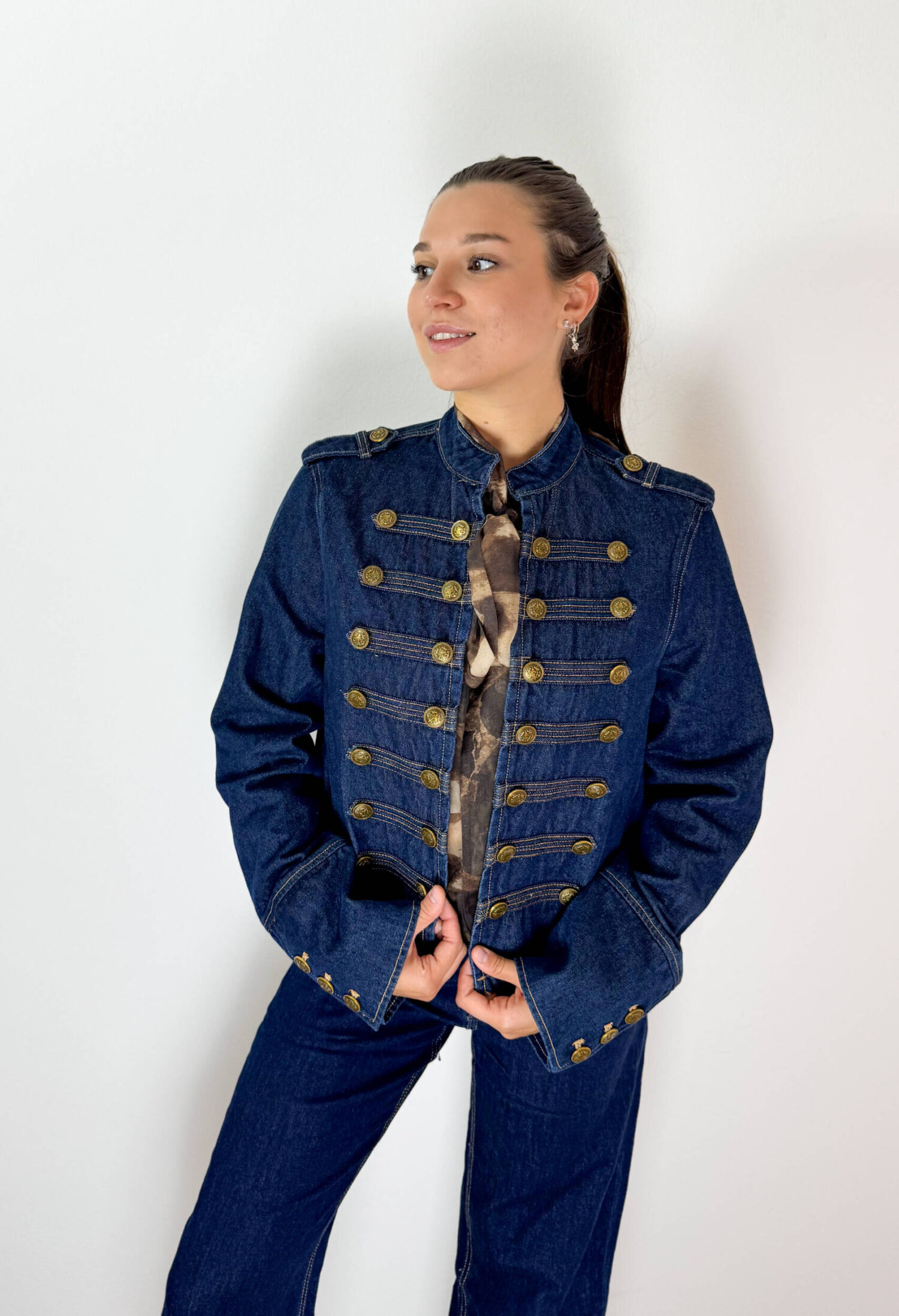 Giacca Denim Napoleonica con Bottoni Dorati Una reinterpretazione contemporanea dell'iconico stile napoleonico, dove il denim incontra dettagli ispirati alle uniformi militari. La giacca in denim presenta una linea strutturata e un'importante lavorazione frontale caratterizzata da bottoni dorati disposti in file, elemento distintivo che cattura subito l'attenzione. Il design richiama l'estetica delle giacche d'ispirazione militare, mantenendo però la versatilità tipica del denim. I dettagli dorati valorizzano il capo e lo rendono particolarmente adatto a chi cerca un'alternativa originale alla classica giacca in jeans. Perfetta con denim coordinato per un total look, ma anche con pantaloni sartoriali, gonne o capi più essenziali. Indossata con sneakers crea un outfit casual e contemporaneo, mentre abbinata a stivali o décolleté si presta a interpretazioni più eleganti.