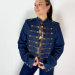 Giacca Denim Napoleonica con Bottoni Dorati Una reinterpretazione contemporanea dell'iconico stile napoleonico, dove il denim incontra dettagli ispirati alle uniformi militari. La giacca in denim presenta una linea strutturata e un'importante lavorazione frontale caratterizzata da bottoni dorati disposti in file, elemento distintivo che cattura subito l'attenzione. Il design richiama l'estetica delle giacche d'ispirazione militare, mantenendo però la versatilità tipica del denim. I dettagli dorati valorizzano il capo e lo rendono particolarmente adatto a chi cerca un'alternativa originale alla classica giacca in jeans. Perfetta con denim coordinato per un total look, ma anche con pantaloni sartoriali, gonne o capi più essenziali. Indossata con sneakers crea un outfit casual e contemporaneo, mentre abbinata a stivali o décolleté si presta a interpretazioni più eleganti.
