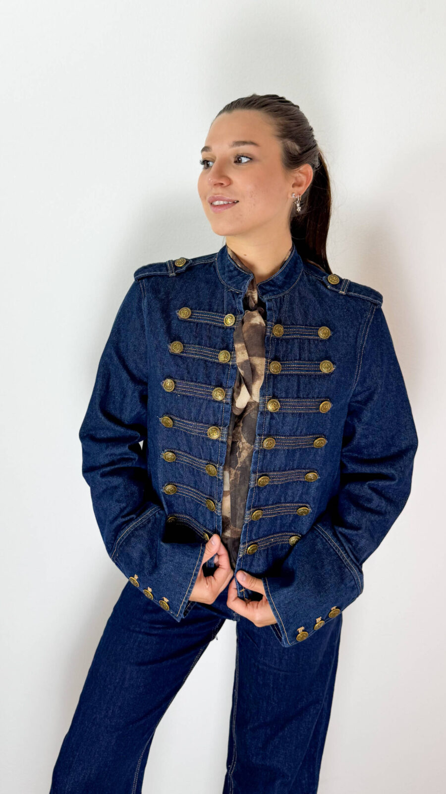 Giacca Denim Napoleonica con Bottoni Dorati Una reinterpretazione contemporanea dell'iconico stile napoleonico, dove il denim incontra dettagli ispirati alle uniformi militari. La giacca in denim presenta una linea strutturata e un'importante lavorazione frontale caratterizzata da bottoni dorati disposti in file, elemento distintivo che cattura subito l'attenzione. Il design richiama l'estetica delle giacche d'ispirazione militare, mantenendo però la versatilità tipica del denim. I dettagli dorati valorizzano il capo e lo rendono particolarmente adatto a chi cerca un'alternativa originale alla classica giacca in jeans. Perfetta con denim coordinato per un total look, ma anche con pantaloni sartoriali, gonne o capi più essenziali. Indossata con sneakers crea un outfit casual e contemporaneo, mentre abbinata a stivali o décolleté si presta a interpretazioni più eleganti.