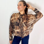Delicata ma ricca di carattere, questa blusa in tessuto velato combina dettagli femminili e una linea contemporanea, creando un equilibrio perfetto tra eleganza e stile sportivo. La fantasia nei toni del marrone con effetto sfumato dona profondità al modello, mentre il fiocco sul collo aggiunge un dettaglio raffinato e distintivo. La vestibilità morbida accompagna la figura con naturalezza, senza segnare, rendendo la blusa piacevole da indossare e facile da abbinare. Le maniche ampie enfatizzano il volume del capo e sono completate da polsini con bottoni, per un tocco più curato e sofisticato. L'elastico sul fondo crea una linea leggermente raccolta, valorizzando la silhouette e conferendo alla blusa un aspetto moderno. Perfetta con pantaloni sartoriali o jeans, si adatta facilmente a diverse occasioni: elegante con un pantalone e un tacco, più casual e contemporanea con denim e sneakers.