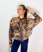 Delicata ma ricca di carattere, questa blusa in tessuto velato combina dettagli femminili e una linea contemporanea, creando un equilibrio perfetto tra eleganza e stile sportivo. La fantasia nei toni del marrone con effetto sfumato dona profondità al modello, mentre il fiocco sul collo aggiunge un dettaglio raffinato e distintivo. La vestibilità morbida accompagna la figura con naturalezza, senza segnare, rendendo la blusa piacevole da indossare e facile da abbinare. Le maniche ampie enfatizzano il volume del capo e sono completate da polsini con bottoni, per un tocco più curato e sofisticato. L'elastico sul fondo crea una linea leggermente raccolta, valorizzando la silhouette e conferendo alla blusa un aspetto moderno. Perfetta con pantaloni sartoriali o jeans, si adatta facilmente a diverse occasioni: elegante con un pantalone e un tacco, più casual e contemporanea con denim e sneakers.