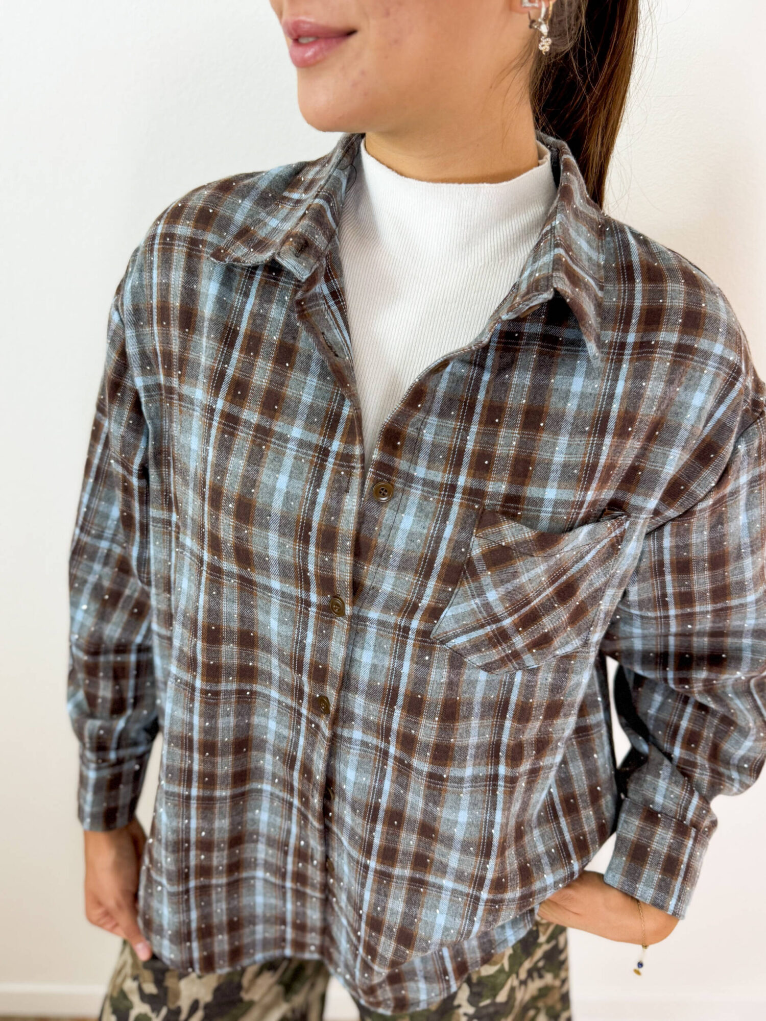 Aggiungi un tocco originale e luminoso ai tuoi outfit con questa camicia a quadretti check con strass applicati, perfetta per chi ama uno stile casual dal carattere deciso. La fantasia check a piccoli quadratini dona al capo un look intramontabile e versatile, mentre gli strass applicati aggiungono un dettaglio brillante e ricercato. Il taschino sul petto completa il design con un elemento funzionale e dal gusto casual. Perfetta da indossare sia aperta sopra una T-shirt sia abbottonata, questa camicia check con strass si abbina facilmente a jeans, pantaloni cargo e bermuda