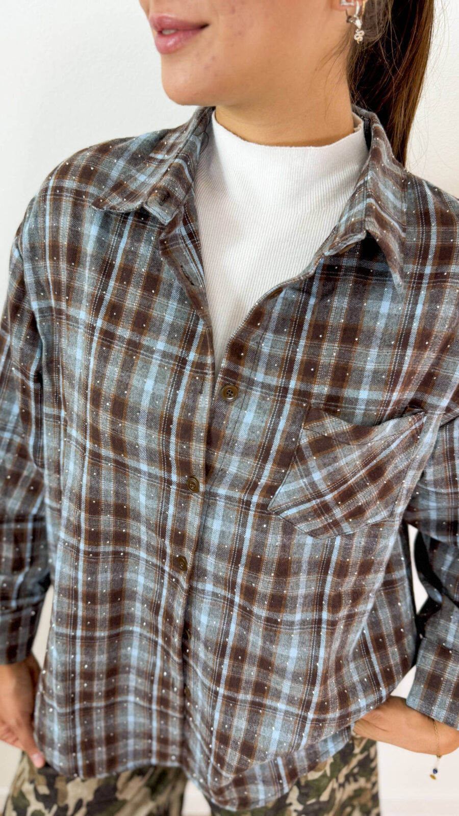 Aggiungi un tocco originale e luminoso ai tuoi outfit con questa camicia a quadretti check con strass applicati, perfetta per chi ama uno stile casual dal carattere deciso. La fantasia check a piccoli quadratini dona al capo un look intramontabile e versatile, mentre gli strass applicati aggiungono un dettaglio brillante e ricercato. Il taschino sul petto completa il design con un elemento funzionale e dal gusto casual. Perfetta da indossare sia aperta sopra una T-shirt sia abbottonata, questa camicia check con strass si abbina facilmente a jeans, pantaloni cargo e bermuda