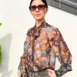 Camicia dalla linea morbida e comoda, caratterizzata da una vivace fantasia floreale nei toni del marrone, ruggine, blu e arancio. Il dettaglio protagonista è il fiocco sul collo, che dona un tocco femminile e originale al modello. La vestibilità fluida la rende facile da indossare e perfetta per creare look semplici ma con carattere. Da abbinare a jeans, pantaloni o gonne, è una camicia versatile ideale per dare un tocco di colore e personalità agli outfit di tutti i giorni.