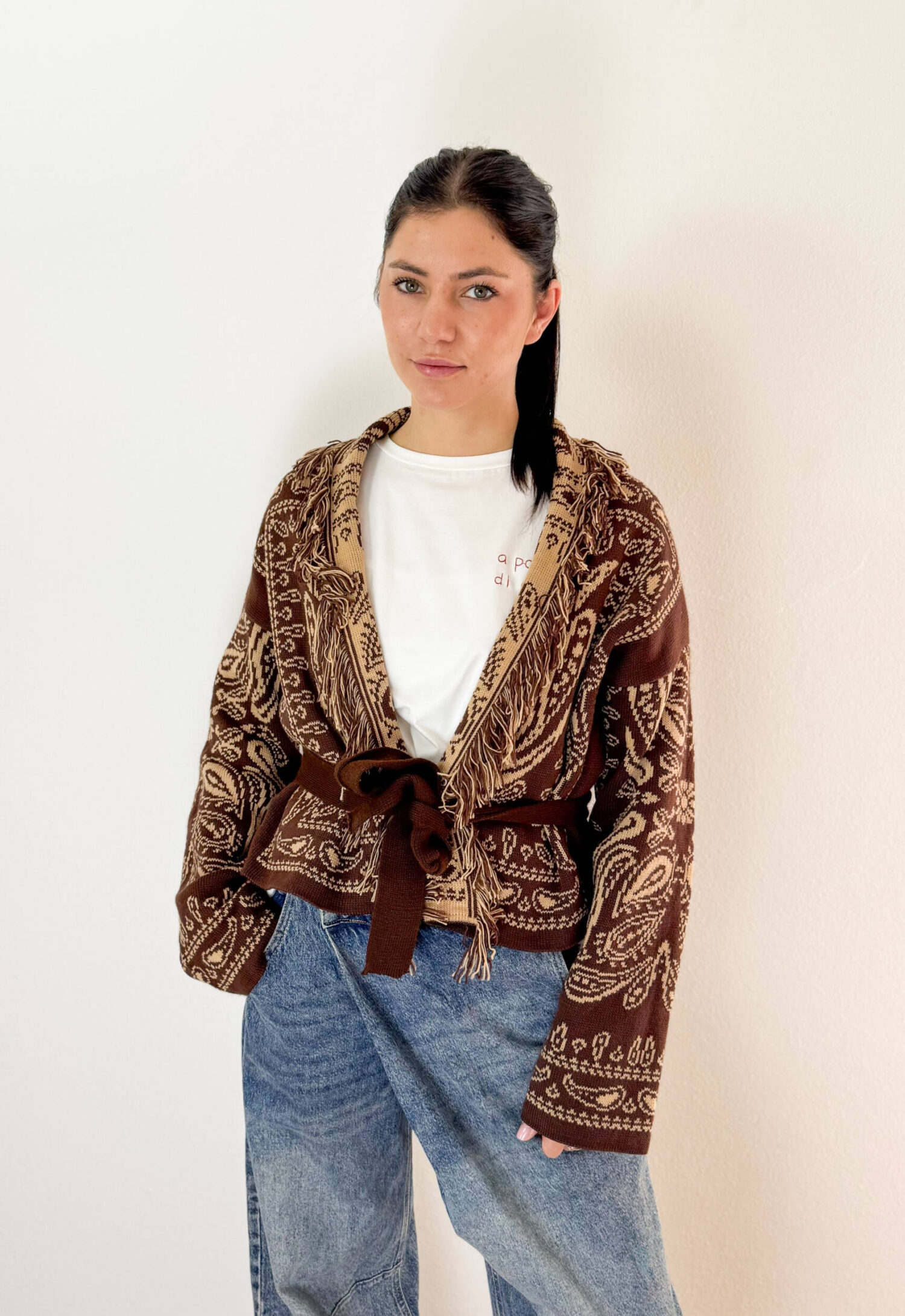 Aggiungi un tocco avvolgente e bohémien al tuo guardaroba con questo cardigan corto dalla finitura etnica. Caratterizzato da un elegante collo a revers impreziosito da dettagli sfrangiati, questo modello aperto sul davanti si distingue per la chiusura con coulisse in vita che permette di sagomare la silhouette a piacimento. Il ricco motivo jacquard su toni caldi del marrone e beige rende ogni outfit raffinato e contemporaneo, perfetto da abbinare a denim a vita alta o pantaloni sartoriali.
