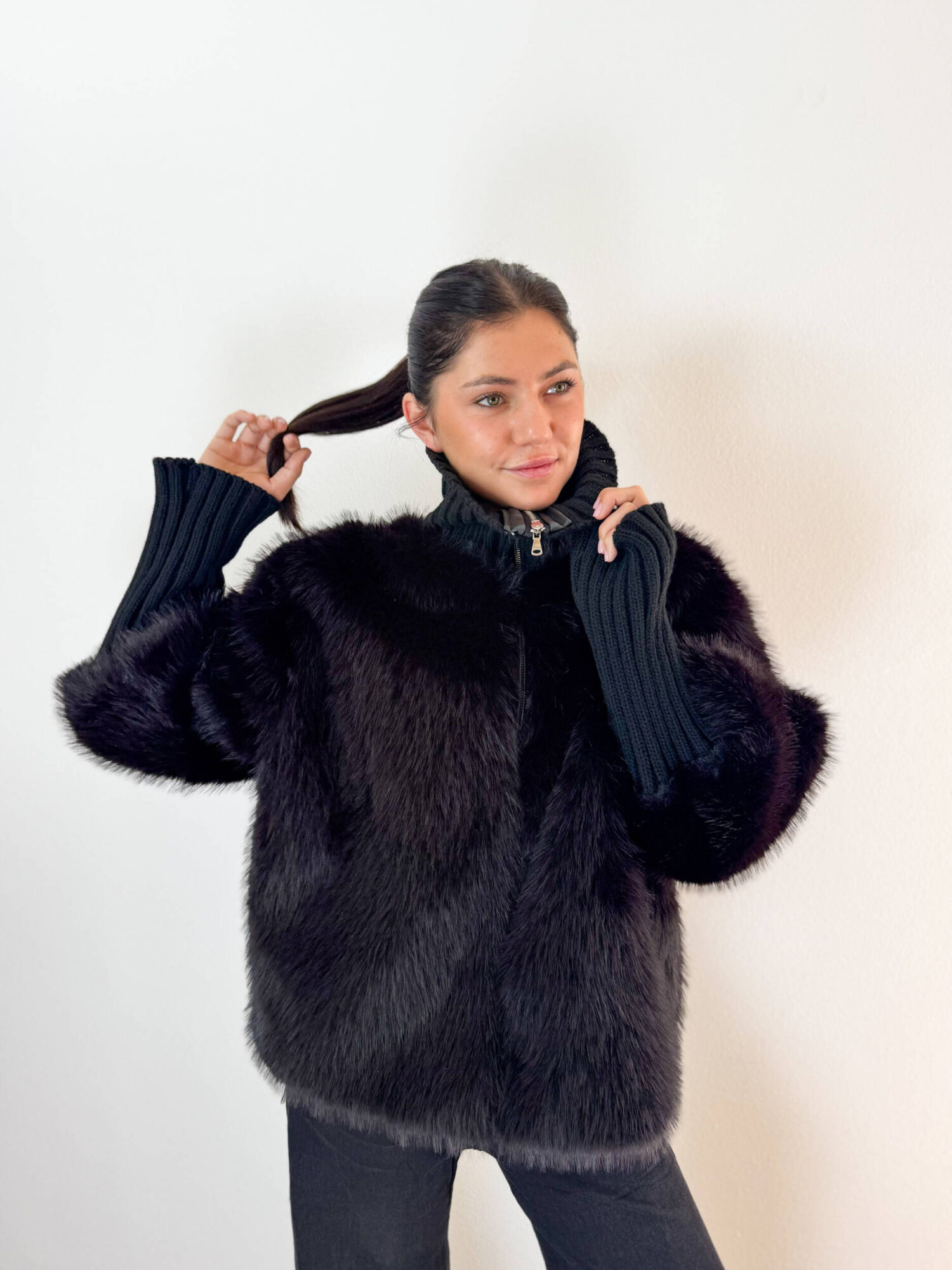 Unisci il lusso avvolgente dell'ecopelliccia alla praticità della maglieria con questa elegante giacca nera, ideale per affrontare le giornate più fredde con uno stile impeccabile. Realizzata con un pelo ecologico morbidissimo e denso, si caratterizza per gli originali ed eleganti inserti in maglia a coste lavorata sul collo alto e lungo le maniche. Il collo alto in maglia protegge dal vento donando un tocco sofisticato, mentre i polsini/maniche elasticizzate a coste assicurano massima aderenza e comfort vestibile. Dotata di una pratica chiusura frontale con zip integrata, è il capospalla perfetto da indossare sia su outfit serali e formali, sia sopra un look casual con jeans per un tocco glamour e contemporaneo.