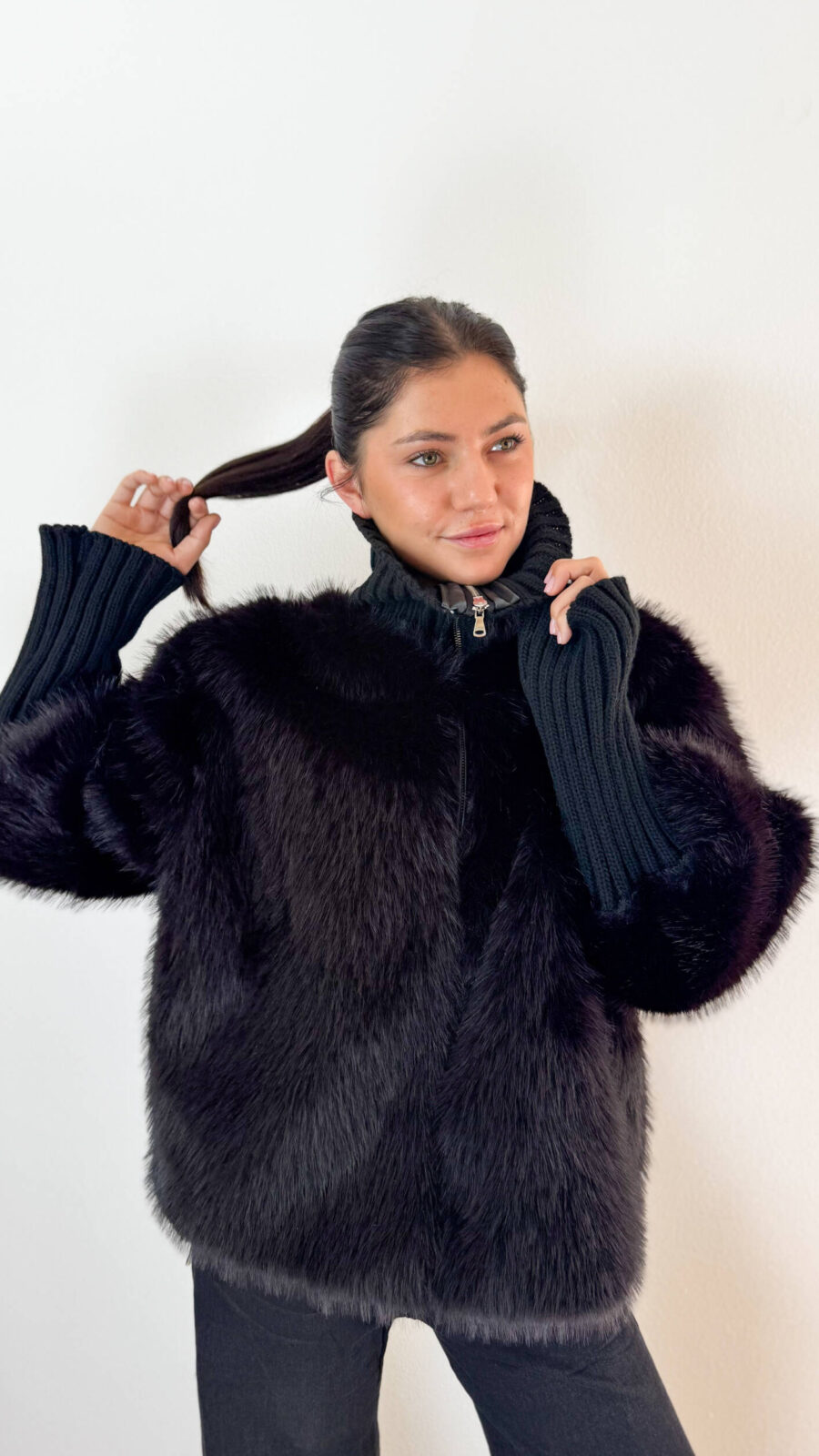 Unisci il lusso avvolgente dell'ecopelliccia alla praticità della maglieria con questa elegante giacca nera, ideale per affrontare le giornate più fredde con uno stile impeccabile. Realizzata con un pelo ecologico morbidissimo e denso, si caratterizza per gli originali ed eleganti inserti in maglia a coste lavorata sul collo alto e lungo le maniche. Il collo alto in maglia protegge dal vento donando un tocco sofisticato, mentre i polsini/maniche elasticizzate a coste assicurano massima aderenza e comfort vestibile. Dotata di una pratica chiusura frontale con zip integrata, è il capospalla perfetto da indossare sia su outfit serali e formali, sia sopra un look casual con jeans per un tocco glamour e contemporaneo.
