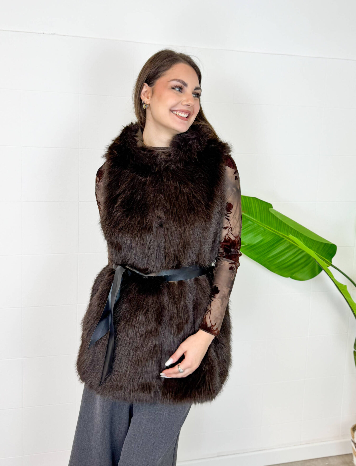 Aggiungi un tocco di raffinatezza e calore ai tuoi outfit invernali con questo gilet smanicato in ecopelliccia marrone scuro. Un capo morbido, avvolgente ed estremamente versatile, ideale per affrontare le giornate più fredde con stile. Dotato di un pratico cappuccio integrato e completamente foderato internamente, garantisce massimo comfort e protezione dal vento. Design e Silhouette: Taglio medio-lungo valorizzato da una cintura nera in vita che definisce la figura regalando una linea elegante e femminile. Dettagli Funzionali: Ampio cappuccio foderato e finitura in eco-pelliccia sintetica ad alta densità, morbida al tatto e dal look lussuoso. Come Abbinarlo: Perfetto indossato sopra una maglia a maniche lunghe, un dolcevita o una camicia trasparente per le serate speciali, abbinato a pantaloni a gamba larga o gonne midi.