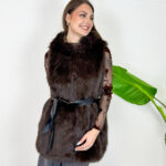Aggiungi un tocco di raffinatezza e calore ai tuoi outfit invernali con questo gilet smanicato in ecopelliccia marrone scuro. Un capo morbido, avvolgente ed estremamente versatile, ideale per affrontare le giornate più fredde con stile. Dotato di un pratico cappuccio integrato e completamente foderato internamente, garantisce massimo comfort e protezione dal vento. Design e Silhouette: Taglio medio-lungo valorizzato da una cintura nera in vita che definisce la figura regalando una linea elegante e femminile. Dettagli Funzionali: Ampio cappuccio foderato e finitura in eco-pelliccia sintetica ad alta densità, morbida al tatto e dal look lussuoso. Come Abbinarlo: Perfetto indossato sopra una maglia a maniche lunghe, un dolcevita o una camicia trasparente per le serate speciali, abbinato a pantaloni a gamba larga o gonne midi.