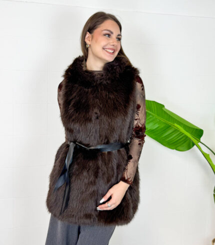 Aggiungi un tocco di raffinatezza e calore ai tuoi outfit invernali con questo gilet smanicato in ecopelliccia marrone scuro. Un capo morbido, avvolgente ed estremamente versatile, ideale per affrontare le giornate più fredde con stile. Dotato di un pratico cappuccio integrato e completamente foderato internamente, garantisce massimo comfort e protezione dal vento. Design e Silhouette: Taglio medio-lungo valorizzato da una cintura nera in vita che definisce la figura regalando una linea elegante e femminile. Dettagli Funzionali: Ampio cappuccio foderato e finitura in eco-pelliccia sintetica ad alta densità, morbida al tatto e dal look lussuoso. Come Abbinarlo: Perfetto indossato sopra una maglia a maniche lunghe, un dolcevita o una camicia trasparente per le serate speciali, abbinato a pantaloni a gamba larga o gonne midi.