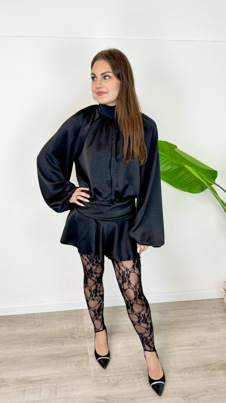 Rendi indimenticabile il tuo outfit con il nostro minidress in rasetto dal fascino sofisticato. Il tessuto satinato, morbido e luminoso, avvolge la figura donando un tocco di eleganza senza tempo. Il design frontale presenta un raffinato colletto rialzato con morbidi drappeggi e maniche lunghe blusanti con polsini stilizzati. Sul retro, il vestito svela un dettaglio inaspettato e sensuale: un'apertura a goccia sulla schiena che si allaccia dietro al collo con delicati bottoncini. Ma il vero segreto di questo abito è la comodità: sotto la minigonna a portafoglio si cela un pantaloncino interno coordinato, studiato per permetterti di ballare, muoverti e vivere la serata in totale disinvoltura e senza pensieri.
