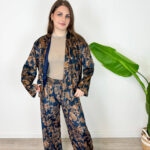 Eleganza lussuosa e massimo comfort si incontrano in questo coordinato due pezzi effetto velluto. Caratterizzato da una raffinata giacca taglio stile kimono aperta sul davanti e pantalone palazzo a gamba larga, questo completino è impreziosito da un'elegante fantasia floreale/barocca su fondo blu scuro e tonalità bronzee. La rifinitura interna in morbido rasetto garantisce una sensazione di estrema piacevolezza e fluidità sulla pelle.