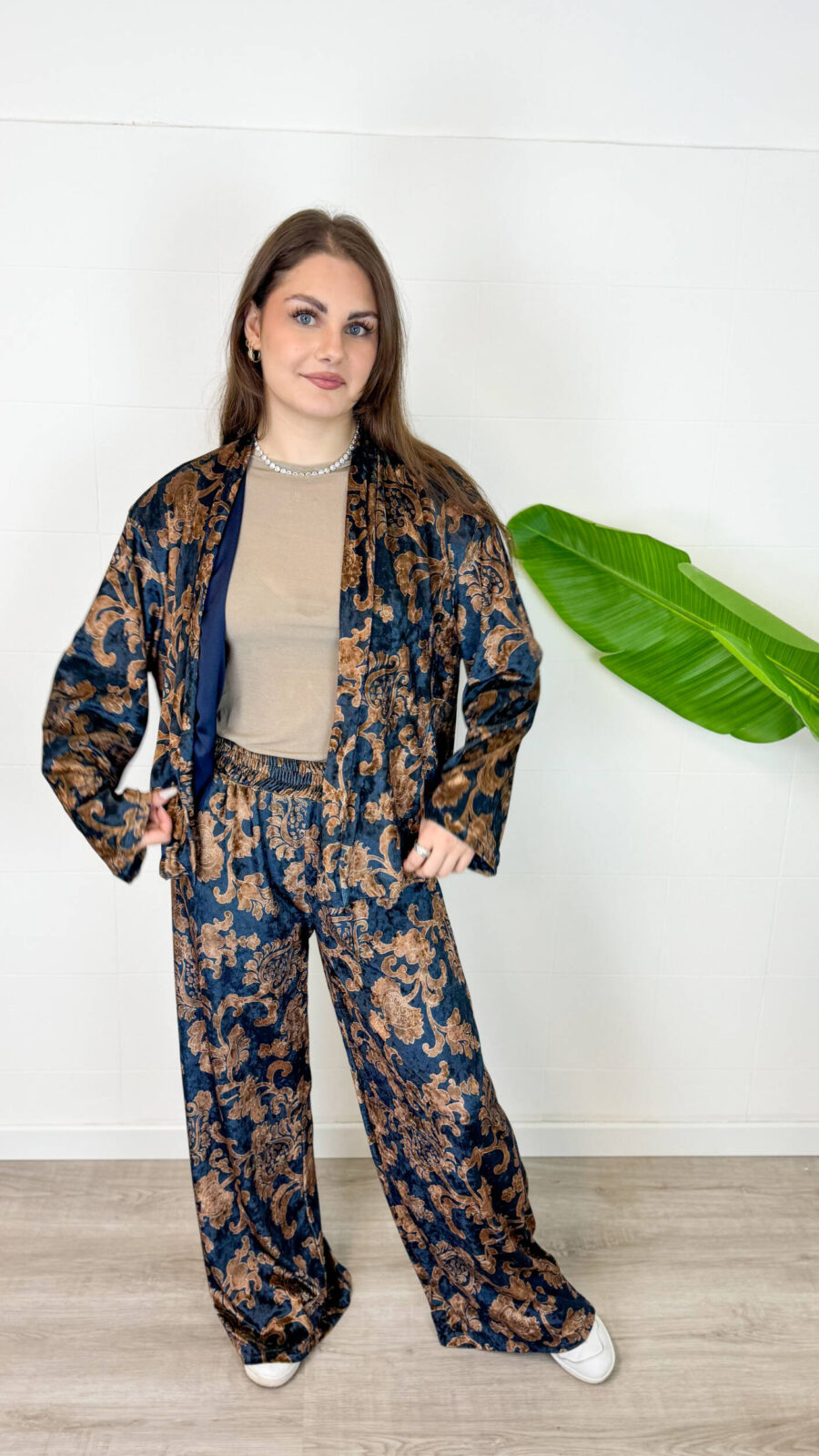 Eleganza lussuosa e massimo comfort si incontrano in questo coordinato due pezzi effetto velluto. Caratterizzato da una raffinata giacca taglio stile kimono aperta sul davanti e pantalone palazzo a gamba larga, questo completino è impreziosito da un'elegante fantasia floreale/barocca su fondo blu scuro e tonalità bronzee. La rifinitura interna in morbido rasetto garantisce una sensazione di estrema piacevolezza e fluidità sulla pelle.