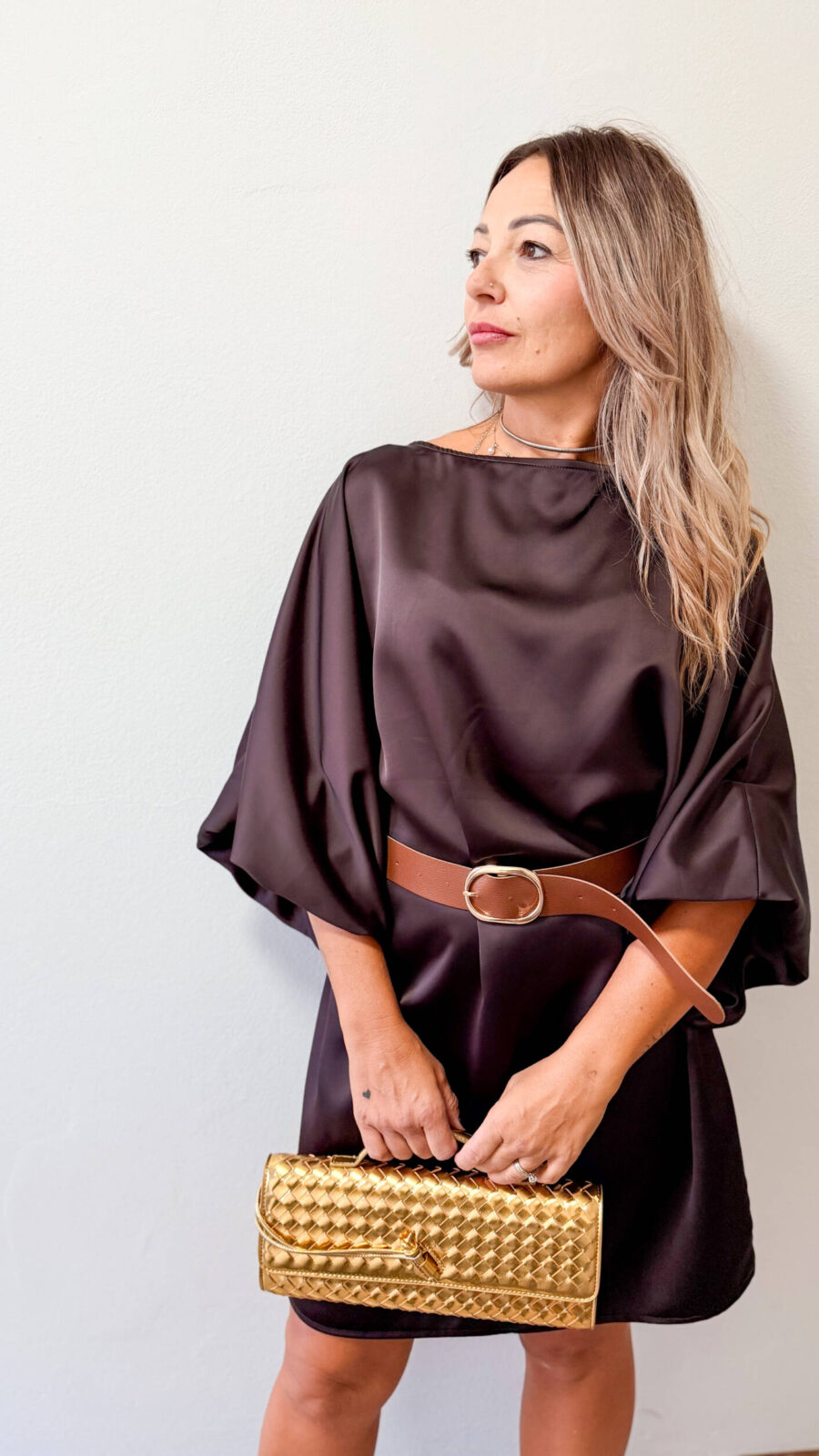Aggiungi un tocco di eleganza senza sforzo al tuo guardaroba con il nostro abito tunica in rasetto lucido. Il tessuto satinato cade delicatamente sulle forme senza segnare, regalando un effetto morbido, luminoso e piacevole al tatto. La linea a tunica dal taglio scivolato è valorizzata da uno scollo a barchetta e da ampie maniche stile kimono/pipistrello a tre quarti, che aggiungono movimento e raffinatezza al capo. Estremamente versatile, è l'abito ideale da sfoggiare sia di giorno che di sera: ti basterà abbinare gli accessori giusti per trasformare completamente il tuo outfit. Dettagli e Caratteristiche:Materiale: Tessuto in rasetto satinato morbido, fluido e luminoso. Design & Scollo: Scollo a barchetta sobrio ed elegante con maniche ampie a tre quarti. Styling Versatile: Indossabile sciolto a tunica oppure sagomato in vita con una cintura. Colori disponibili: Marrone cioccolato e Nero classico. Taglie e Vestibilità: Vestibilità comoda ed elastica, adatta dalla taglia M alla XL.